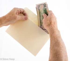 Caucasian ethnicity hands putting fifty dollar bills in envelope