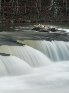 Heavily flooded Tygart Valley river flows in smooth slow motion image over waterfall in Valley Falls State Park West Virginia