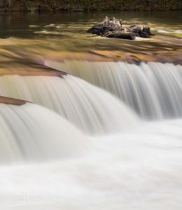 Heavily flooded Tygart Valley river flows in smooth slow motion image over waterfall in Valley Falls State Park West Virginia