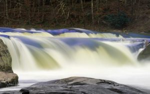 Heavily flooded Tygart Valley river flows in smooth slow motion image over waterfall in Valley Falls State Park West Virginia