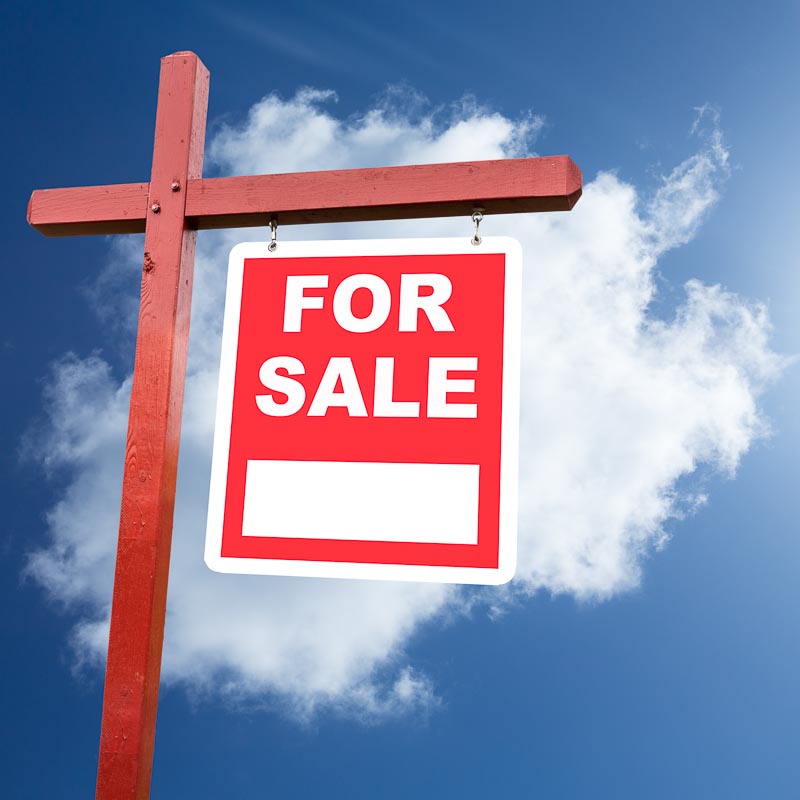 Realtor installed for sale sign for house or real estate set against blue sky and clouds