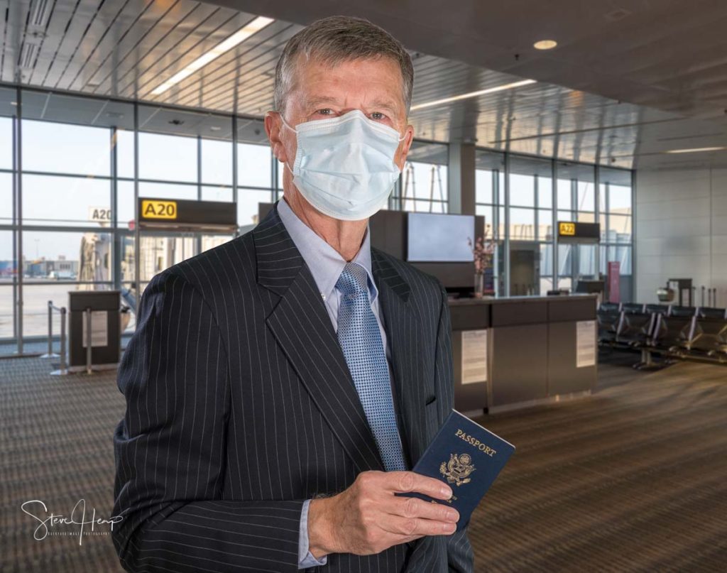 Stock photo of senior businessman ready for travel with face mask and passport
