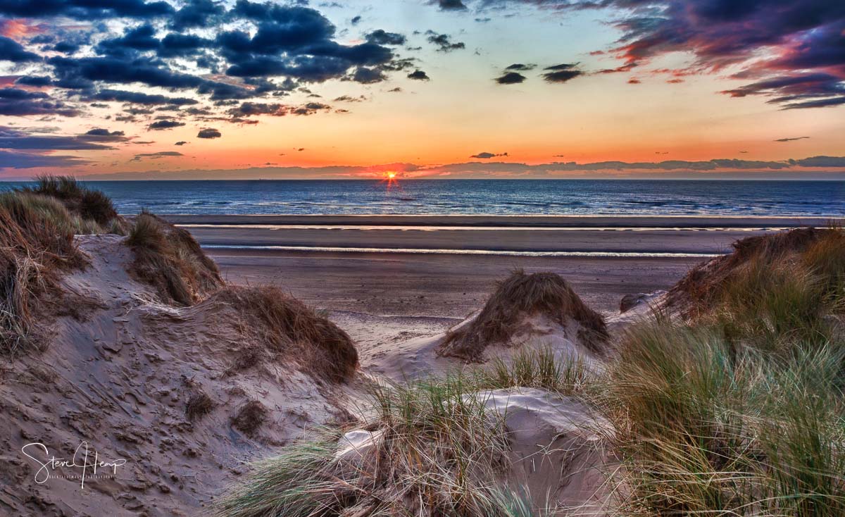 Sun setting over the beach at Formby in England through sand dunes. 